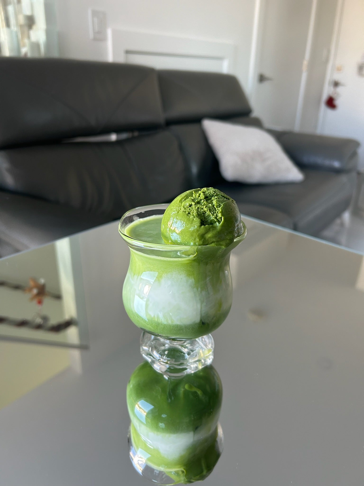 Green Matcha dessert in a glass on a reflective surface with a blurred indoor background